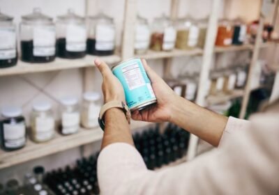 Shopper reading a product label on a tin can in a shop lined with glass storage jars, illustrating retail labeling tips