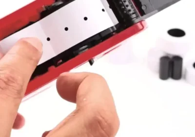 Hands clearing a label jam in a red Easy Tag price gun